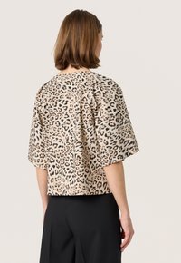 Majica s kratkim rukavima u leopard uzorku s labavim krojem, izrađena od teksturiranog bež materijala. Dizajn s izrezom na leđima s vidljivim šavovima.