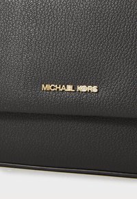 Fekete bőrtáska, textúrált felülettel, arany színű "MICHAEL KORS" logóval. A dizájn letisztult vonalakkal és minimális díszítésekkel rendelkezik.