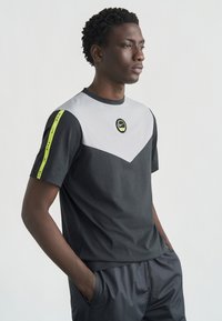 Κοντομάνικη μπλούζα Nike με μαύρο ύφασμα, γκρι πάνελ σε σχήμα V και νέον πράσινες λεπτομέρειες στα μανίκια, λογότυπο στο κέντρο και άνετη εφαρμογή.