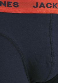 Dunkelblaue Baumwollunterhose mit einem breiten roten elastischen Bund, auf dem der Text "JACK & JONES" steht. Die Textur ist glatt mit sichtbaren Nähdetails.