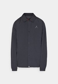 Veste noire légère avec fermeture à boutons, petit logo argenté sur la poitrine gauche, poignets élastiques et col classique, présentée sur fond blanc.