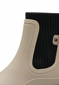 Bottes de cheville en beige imperméables avec un dessus en tissu noir côtelé, présentant un bord cousu et un accent circulaire décoratif.