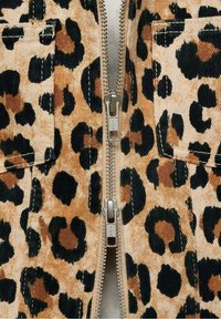 Sako s leopardím vzorem na zip, vyrobené z texturované látky v odstínech béžové, černé a hnědé. Obsahuje náprsní kapsy.