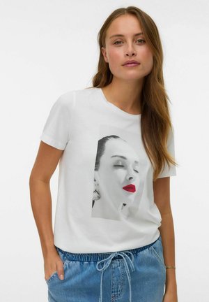 Kvinde med langt hår iført en hvid t-shirt med et sort-hvidt close-up portræt af et ansigt med røde læber, kombineret med blå cowboybukser.