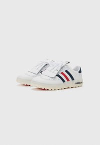 Vita sneakers i strukturerat läder, med röda och marinblå ränder, perforerade detaljer och en kraftig gummisula. Adidas-logotyp synlig.