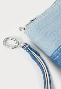Light blue denim wallet with silver hardware, featuring a zipper closure and a blue strap with white stitching for added detail.