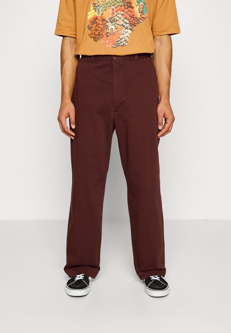 Bordeaux jeans med rak bendesign, prydda med en framficka och en knappstängning. Bärs med en brun T-shirt och svarta sneakers.