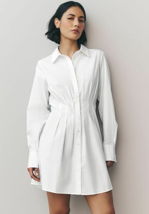 Witte jurk van katoen, met een knoopsluiting aan de voorkant, lange mouwen, een aansluitende taille en geplooide details in de rok.