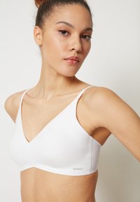 White wireless bra made of smooth fabric, featuring a deep V-neckline, narrow straps, and a subtle logo at the side.