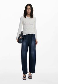 Weißes Strickoberteil mit langen Ärmeln, weite Jeanshose und marineblaue Plateau-Sandalen. Besondere Details: Zopfstrickstruktur und Knopfbund.