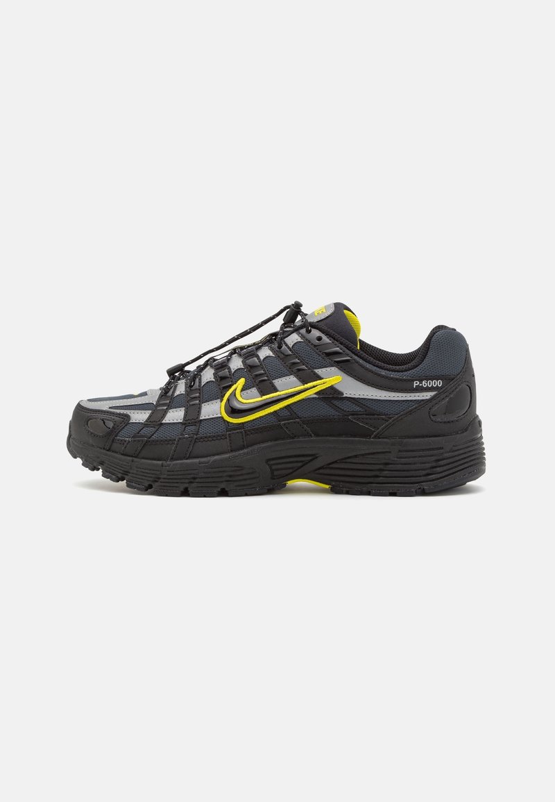 Baskets Nike P-6000 noires et grises avec des accents jaunes, logo Swoosh latéral et lacets noirs sur fond blanc uni.