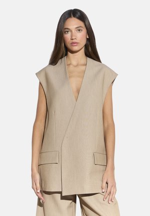 Beiger ärmelloser Blazer mit tiefem V-Ausschnitt, zwei Vorder-taschen und einer strukturierten Gestaltung. Hergestellt aus strukturiertem Stoff. Minimalistischer Stil.