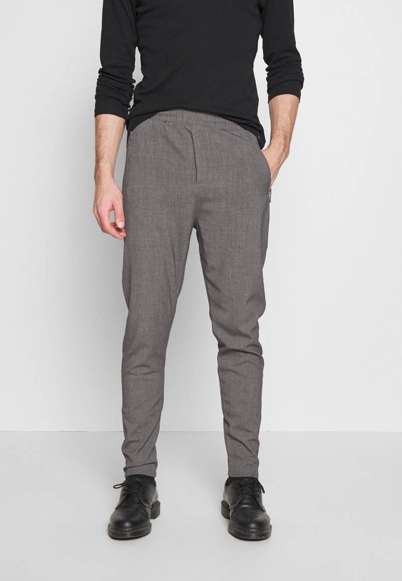 Grå vävda byxor med smal passform, som har ett elastiskt midjeband och sidofickor, kombinerade med svarta skor och en långärmad svart skjorta.