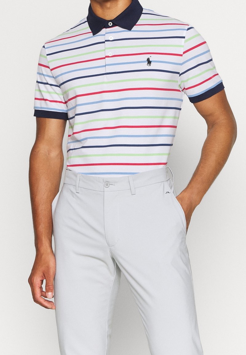 Camisa tipo polo con rayas horizontales multicolores (rojo, verde, azul) y cuello azul marino. Combinada con pantalones gris claro, cuenta con un logo en la camiseta.