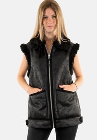 Chaleco negro sin mangas con un acabado texturizado, cuello de piel, cierre frontal con cremallera y dos bolsillos frontales. Acentuado con ribetes negros y hebillas.