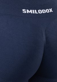 Close-up van marineblauwe leggings met de merknaam "SMILODOX" in het wit op de tailleband, waarbij de textuur en pasvorm van de stof zichtbaar zijn.