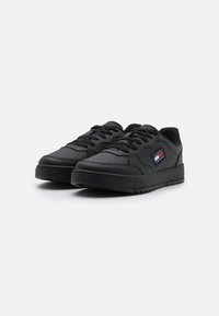 Scarpe sportive nere realizzate in materiale sintetico liscio. Presentano un'area della punta perforata, un design con lacci e una suola in gomma testurizzata.