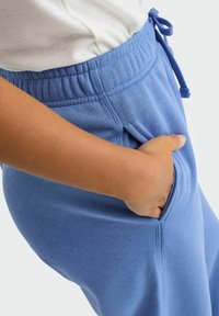 Lyseblå joggers lavet af blødt stof, med elastisk talje og snor, sidelommer og en glat overflade.
