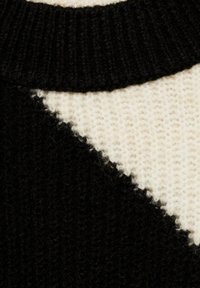 Pull en tricot présentant un contraste de couleurs noir et crème. Motif triangulaire notable au niveau du col. Tissu texturé et doux.