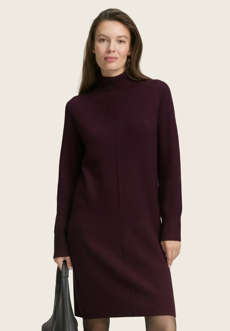Burgunderrotes Strickkleid mit hohem Kragen und langen Ärmeln, das ein schlankes Design und eine gerade Silhouette aufweist, getragen mit einer schwarzen Tasche.