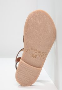 Semelle de sandale en cuir marron avec texture antidérapante. Présente le nom de la marque gravé ainsi que la taille sur une base en caoutchouc léger.