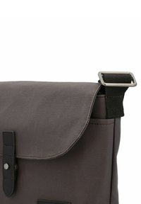 Grijze stoffen tas met een klepafsluiting, zwarte accenten en zilverkleurige metalen hardware. Beschikt over een gestructureerd oppervlak en een zijhandvat.