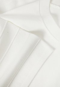 Tissu blanc doux avec des poignets côtelés sur un vêtement à manches longues, montrant la texture et les détails fins du tricot.