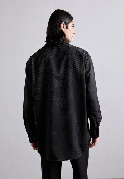 Schwarzes Langarmshirt mit strukturiertem Muster. Verfügt über einen spitzen Kragen und Knopfmanschetten. Die Rückansicht zeigt eine lockere Passform und einen abgerundeten Saum.