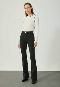 White long-sleeve top with black trim, paired with high-waisted black flared jeans. Smooth fabric, fitted design, and two front pockets.