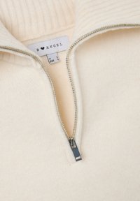 Cremfarbener Reißverschluss-Pullover mit geripptem Kragen, glatter Textur, silbernem Reißverschluss und sichtbar eingesticktem Markenlabel.