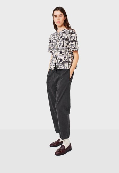 Short-sleeve patterned shirt in cream with navy geometric designs, paired with loose dark gray trousers and burgundy loafers.