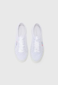 White lace sneakers featuring a floral pattern, satin laces, and a rubber sole with a subtle branding accent on the side.