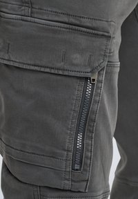 Graue Cargo-Hosen mit strukturiertem Finish, ausgestattet mit einer Reißverschlusstasche an der Seite, verstärkten Nähten und einem sicheren Druckknopfverschluss an der Klappe.