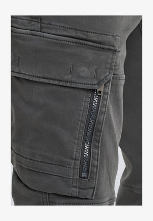 Pantaloni cargo grigi con una finitura testurizzata, dotati di una tasca con zip sul lato, cuciture rinforzate e una chiusura a scatto sicura sulla patta.