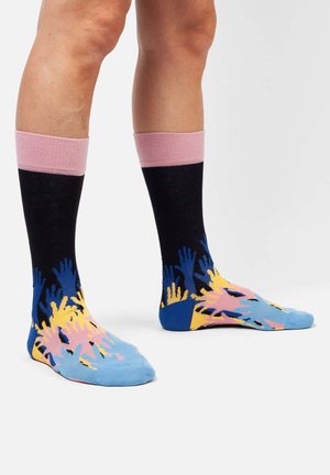 Wadenlange Socken mit einem pinken Rippbündchen, schwarzem Schaft und blauer Fußpartie, verziert mit bunten Handmustern in Gelb und Pink. Weicher Stoff.