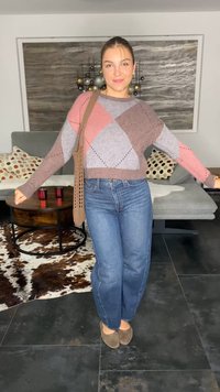 Strickpullover mit geometrischen Mustern in Rosa, Grau und Braun; kombiniert mit hochgeschnittenen blauen Jeans und einer beigefarbenen Umhängetasche.