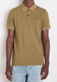 Polo vert olive en coton, avec col, patte de boutonnage à trois boutons et petit logo sur la poitrine. Manches courtes et coupe régulière.