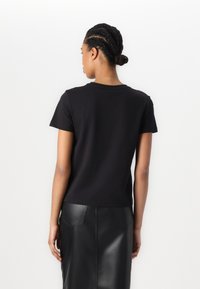 T-shirt nera in cotone con maniche corte, scollo rotondo e orlo dritto, abbinato a una gonna in pelle a vita alta.