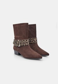 Bottes de cheville en daim marron avec des orteils pointus, présentant une sangle à motif léopard et une boucle en argent, reposant sur un petit talon carré.