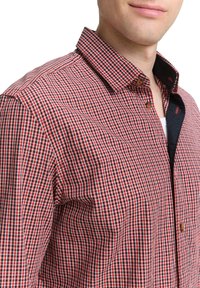 Rot-schwarz kariertes Hemd mit Button-Down-Kragen, kleinen Knöpfen und strukturiertem Stoff. Seitenansicht, die die Passform und die Kragendetails zeigt.