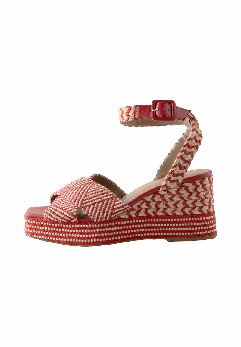 Sandale à talon compensé tressée rouge et beige avec bride de cheville, boucle et brides croisées à l'avant, sur fond blanc.