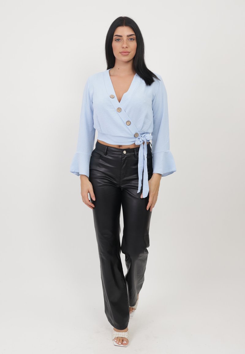 Un haut croisé à manches longues de couleur bleu clair avec un col en V, trois grands boutons et un lien à la taille, associé à un pantalon en cuir noir taille haute.