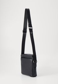Bolso de hombro sintético negro con superficie texturizada, correa ajustable, forma rectangular y bolsillo delantero con cremallera.
