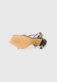 Tacco a stiletto in vernice nera con suola in tan testurizzato. Caratterizzato da un design a tacco quadrato e hardware dorato per una vestibilità regolabile.