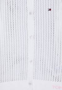 Cárdigan blanco de punto con un tejido ligero y abierto, cinco botones y un pequeño logo en rojo y azul marino. Puños y dobladillo acanalados.