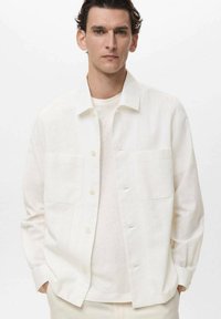 White, long-sleeve button-up shirt in lightweight fabric with two chest pockets, relaxed fit, and subtle texture. Worn over a light shirt.