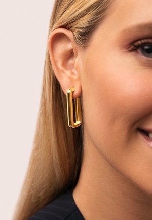Pendientes de aro de metal dorado con un diseño rectangular, acabado brillante y textura suave, colgados de la oreja de un modelo.