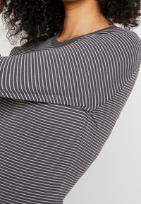 Mörkgrå långärmad topp i tyg med vita horisontella ränder, rundad halsringning och en figurnära design som framhäver armformen.