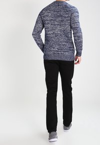 Suéter de punto texturizado azul marino con cuello redondo y mangas largas, combinado con pantalones negros y zapatillas grises, visto desde atrás.