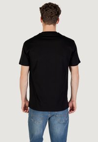 Must t-särk mustast puuvillast lühikeste varrukatega; sile tekstuur ja ümmargune kaelus. Kandmisel siniste teksadega, vaade seljalt.